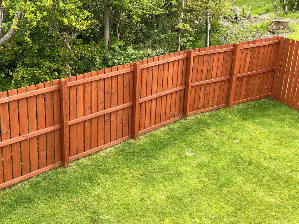 A wood fence being stained with an oil-based finish