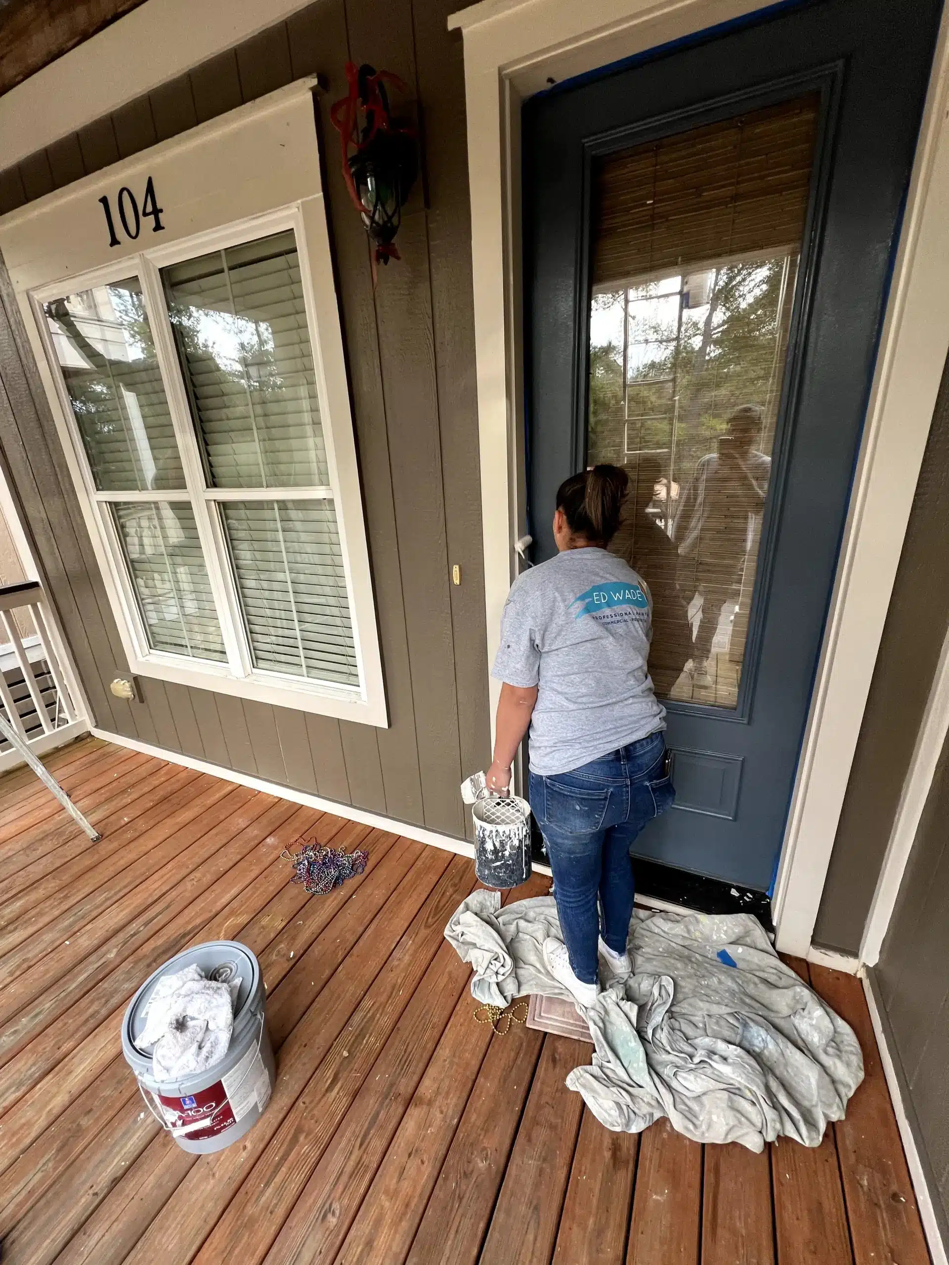 Residential Front Door Painting and Entryway Refresh A painter carefully applying dark blue paint to a residential front door on a brown house.