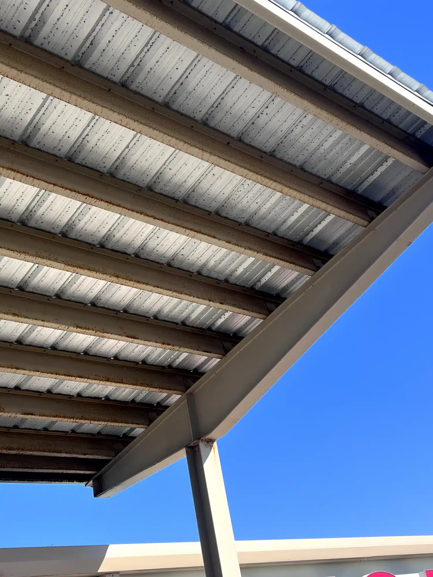 Painted Patio Ceiling And Beams Tan painted patio ceiling with white metal corrugated roof panels and exposed beam structure against clear blue sky